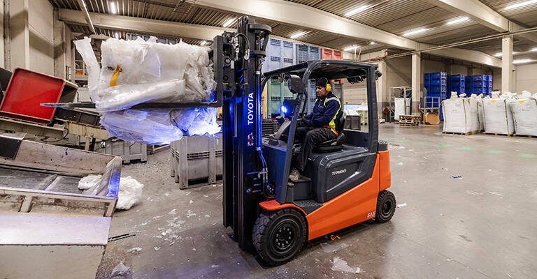 Heftruckchauffeur vervoert een baal met recyclage afval aan een productieband met een Toyota traigo48 elektrische heftuck