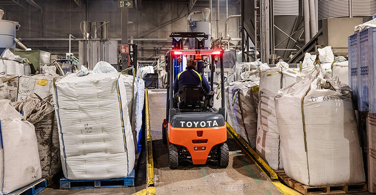 Chariot élévateur électrique Toyota Traigo80 circulant sur une rampe dans un environnement de production dédié au recyclage des déchets.