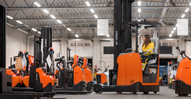 Forklift operator driving Toyota reach truck in warehouse with rental and used trucks